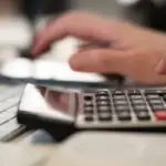 Close-up of hands using a calculator and keyboard in a financial setting, indoors.